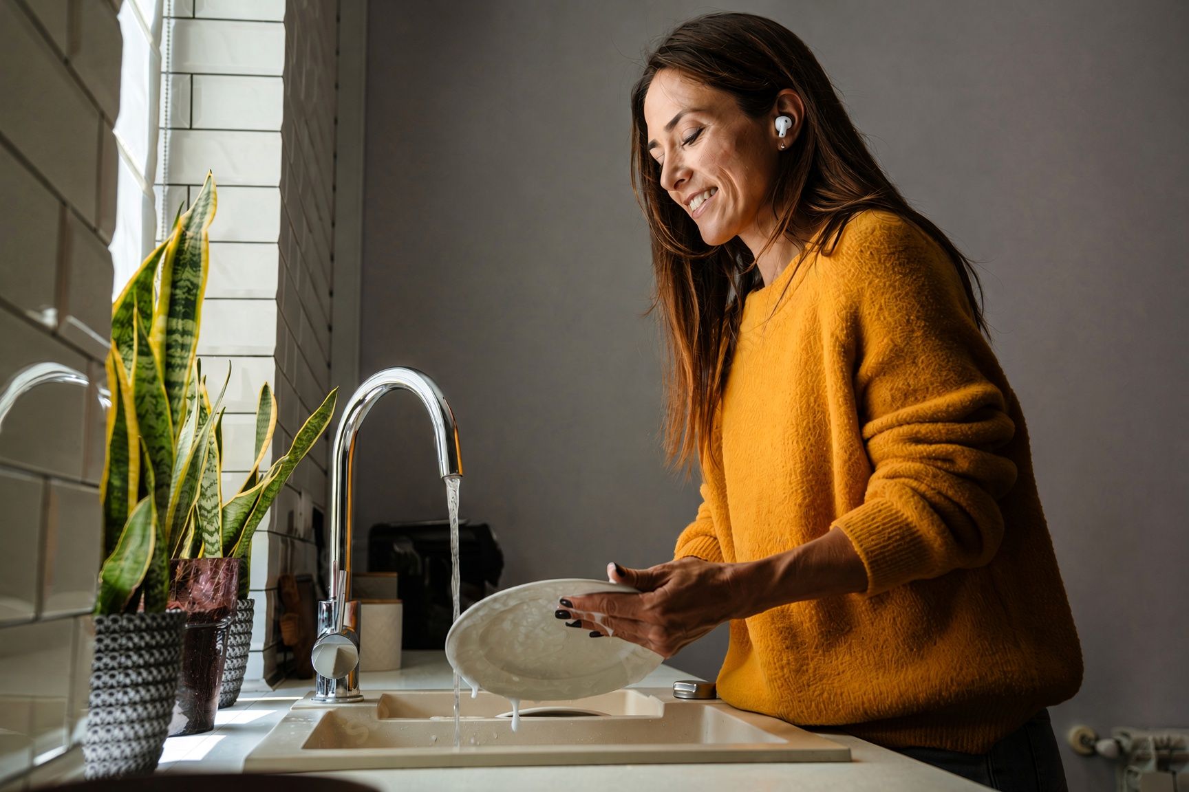 A woman listening with earbuds while washing dishes